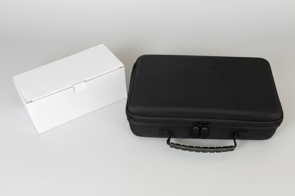 Black hard-shell travel case next to a white rectangular box on a gray concrete floor.
