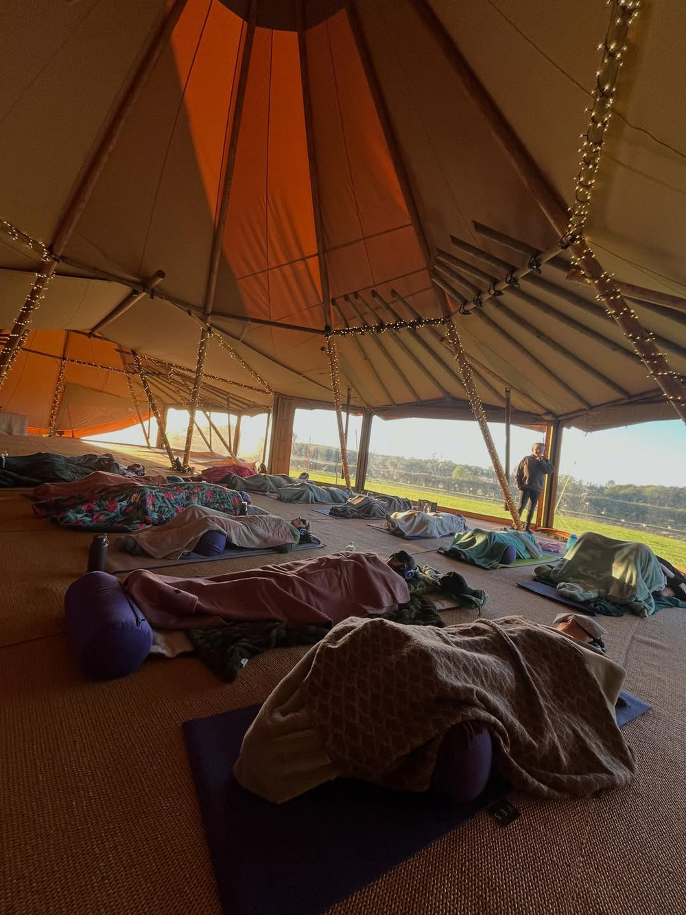 Inside a large tent with people lying on mats and blankets, possibly at an event or gathering.