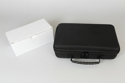 Black hard-shell travel case next to a white rectangular box on a gray concrete floor.